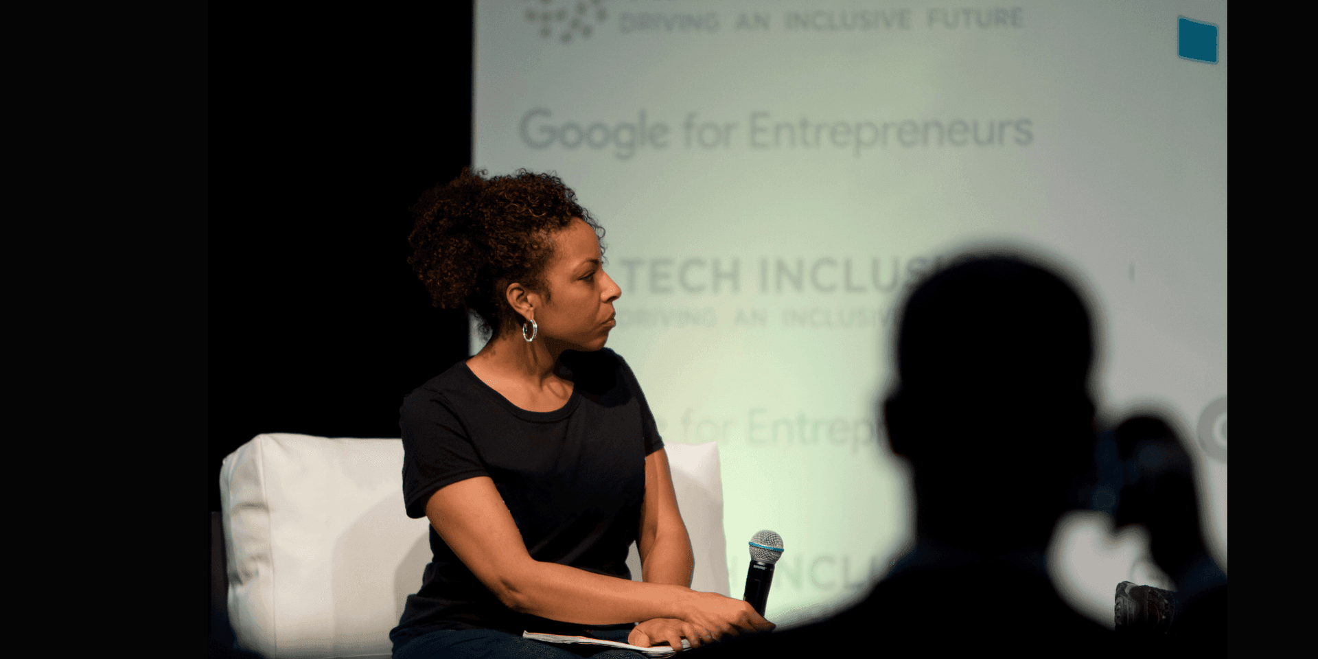 Image of Cynthia Overton sitting on a white chair and holding a microphone.