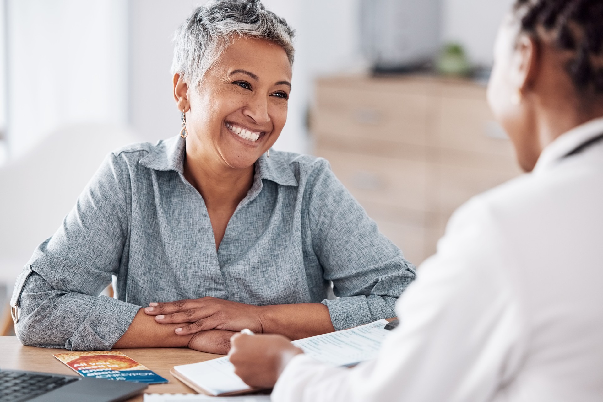 Paperwork, doctor or consulting a happy patient in meeting talking in hospital for history or healthcare record. Smile, medical or nurse with mature woman speaking of test results, update or document